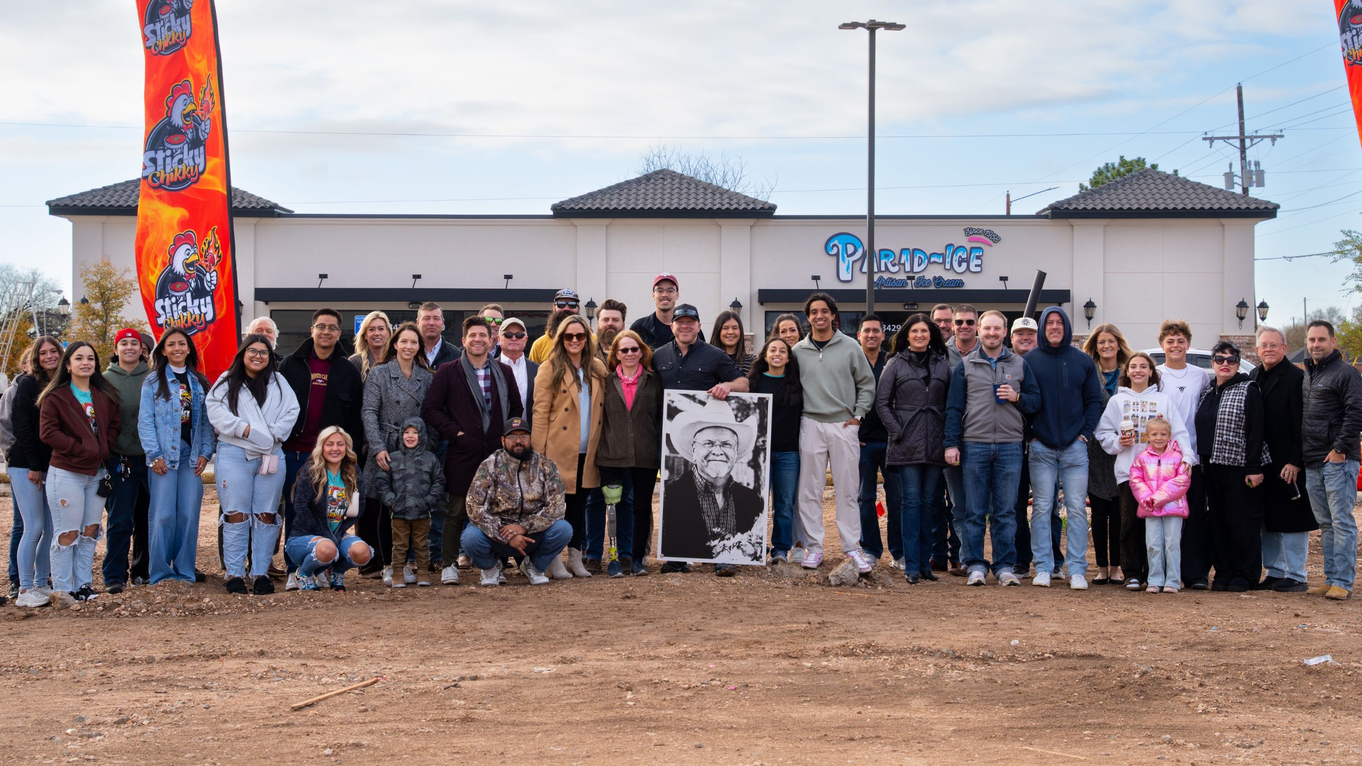 The Sticky Chikky community gathered at the Osage groundbreaking, with Sticky Chikky branded banners and a portrait of Jimmy Snider