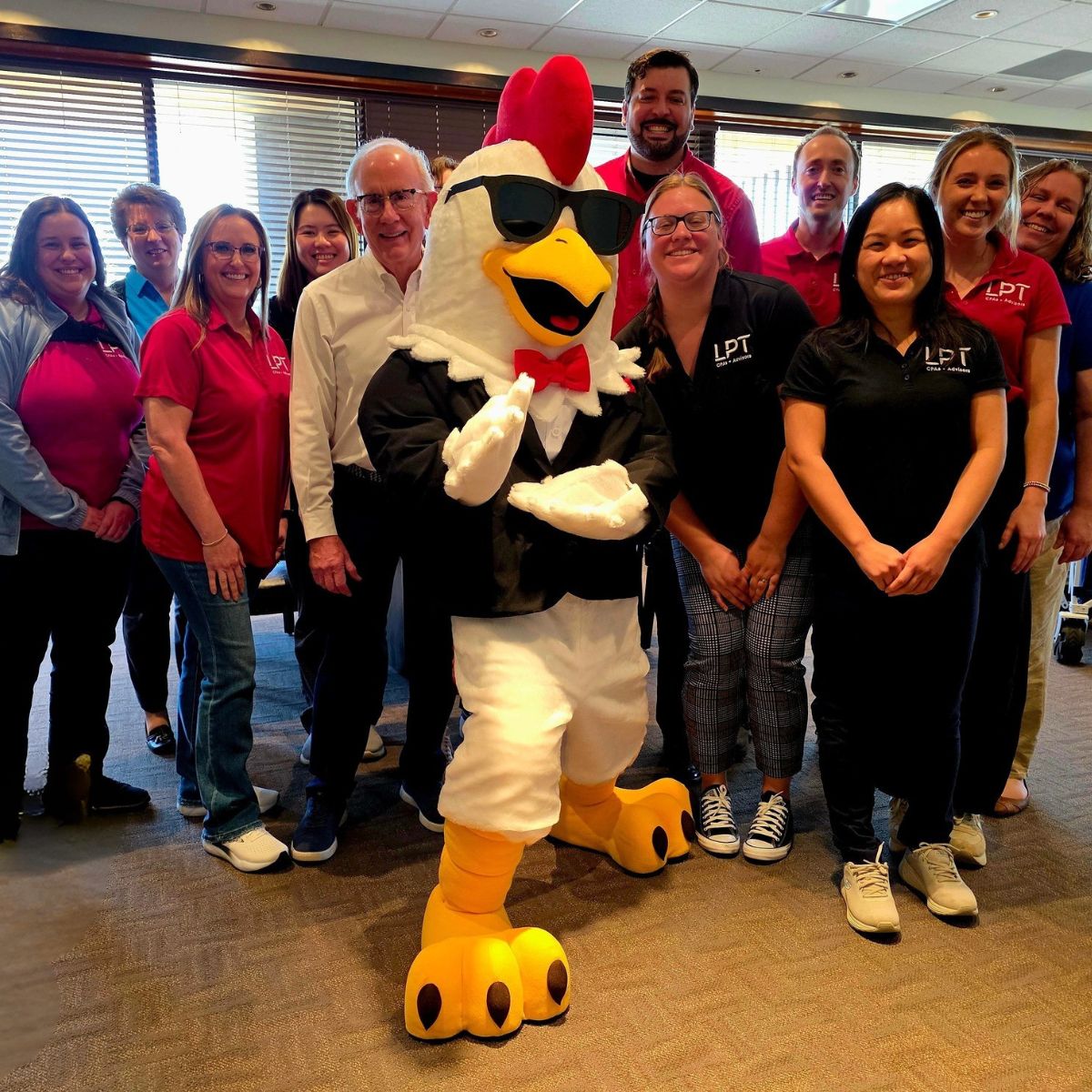 The Sticky Chikky chicken mascot in sunglasses posing with a large group of people wearing LPT-branded shirts at a catering event
