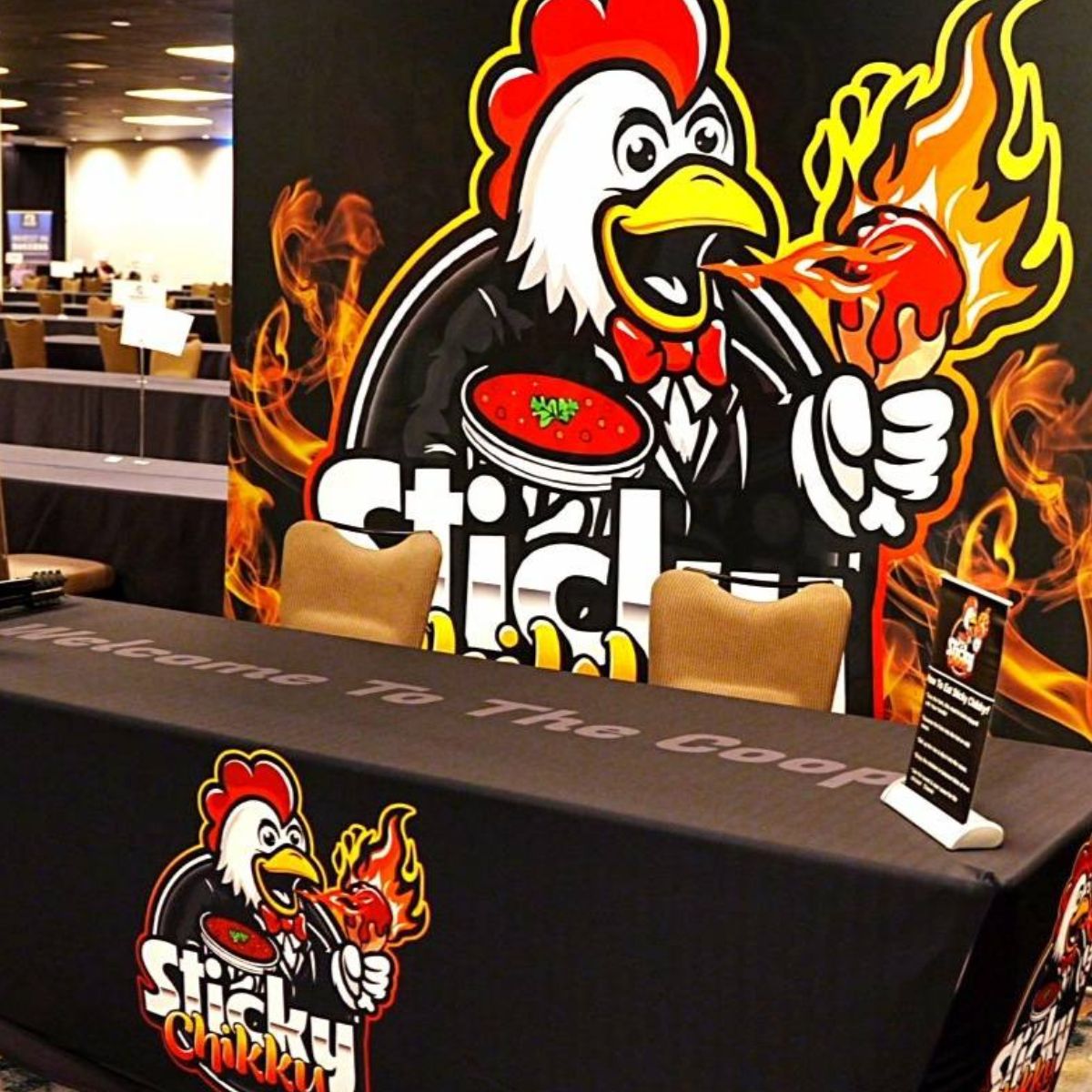 Sticky Chikky trade show booth with a large mascot backdrop and a "Welcome To The Coop" branded table cover in a conference hall