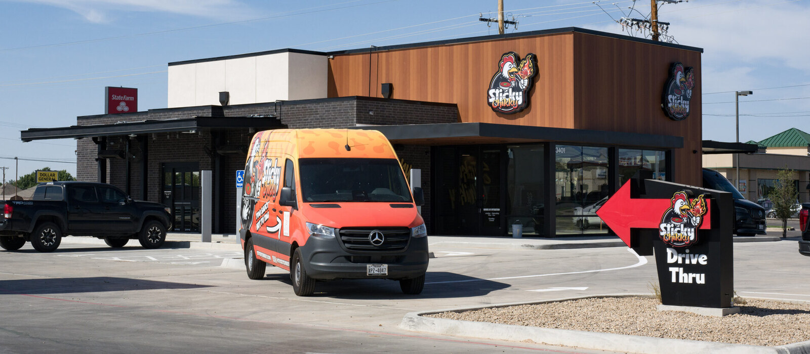 Finished Sticky Chikky storefront at 34th and Osage, with illuminated signs, branded delivery van, and drive thru sign