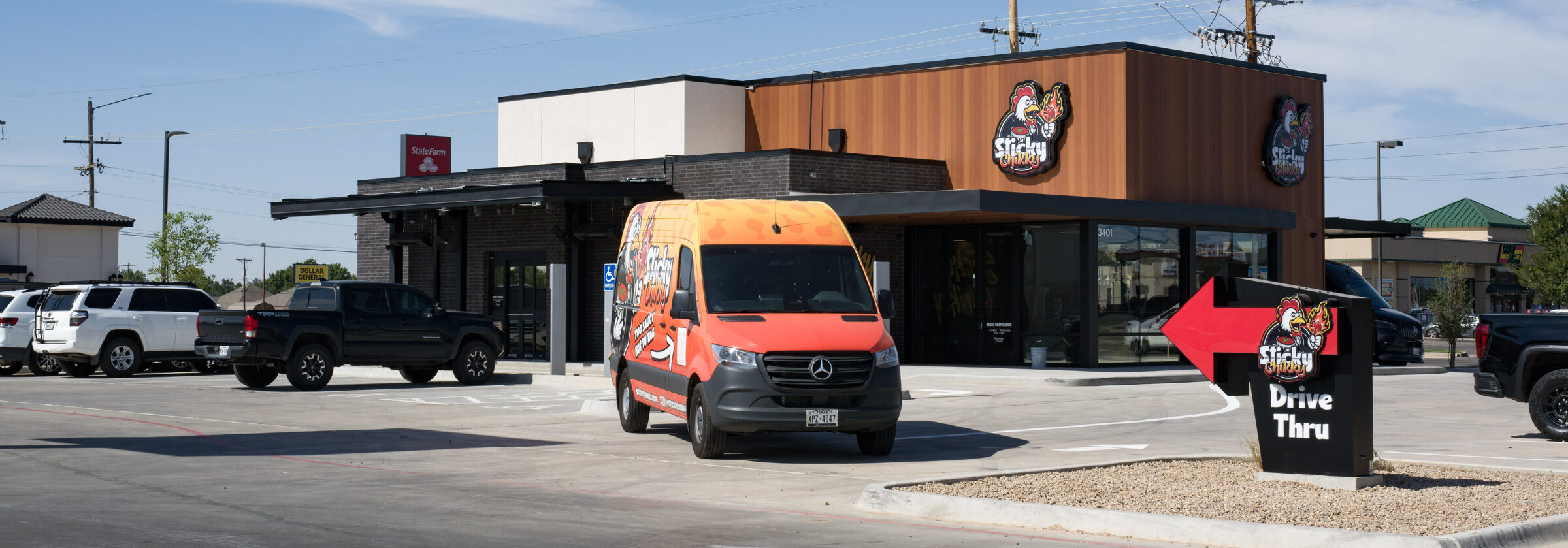 Finished Sticky Chikky storefront with illuminated signage on two elevations, a branded delivery van in the parking lot, and a drive thru directional sign.