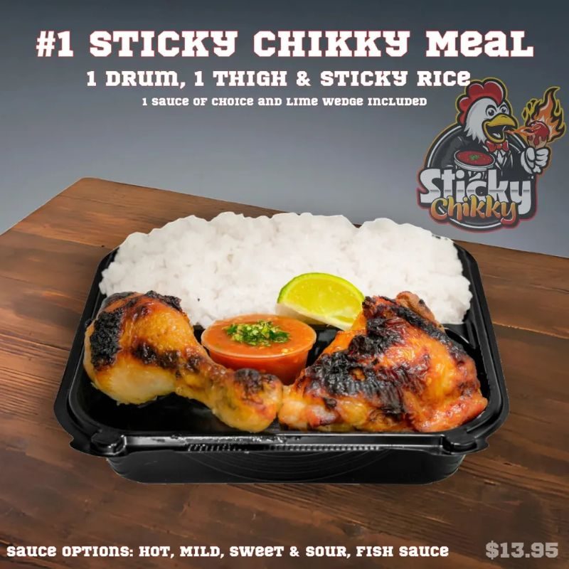 A black meal box with one drumstick and one thigh over sticky rice, a red sauce cup garnished with herbs, and a lime wedge