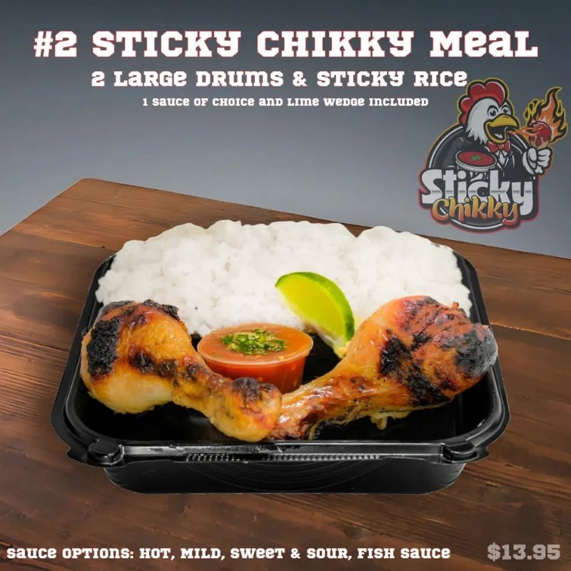 A black meal box with two drumsticks over sticky rice, a red sauce cup garnished with herbs, and a lime wedge