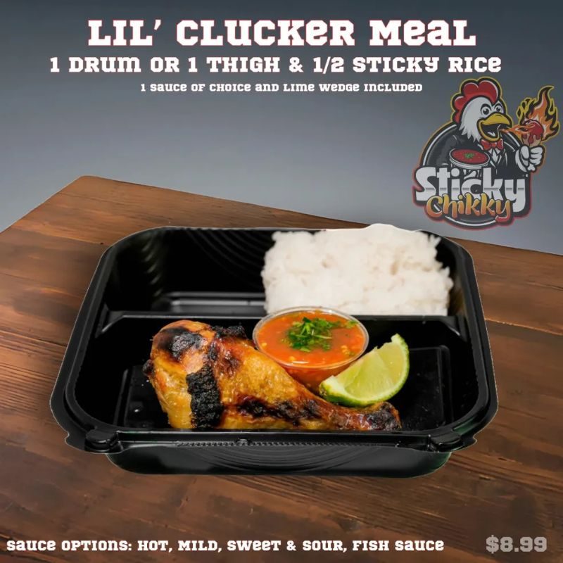 A black meal box with one drumstick over sticky rice, a red sauce cup, and a lime wedge
