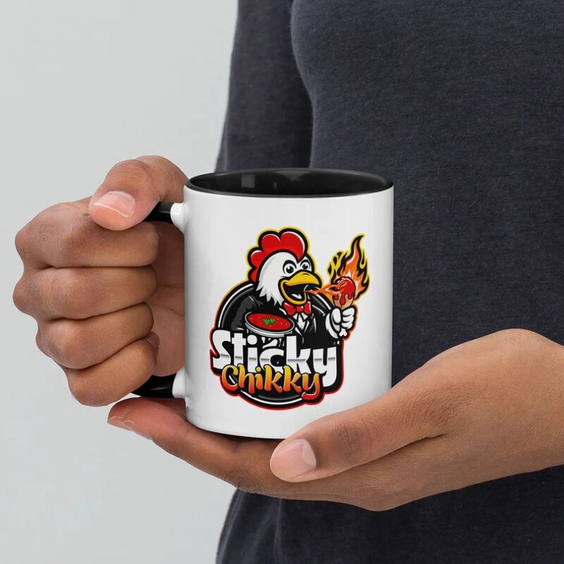 Hands holding a white ceramic mug with a black interior and handle, featuring the Sticky Chikky mascot character logo printed on the side