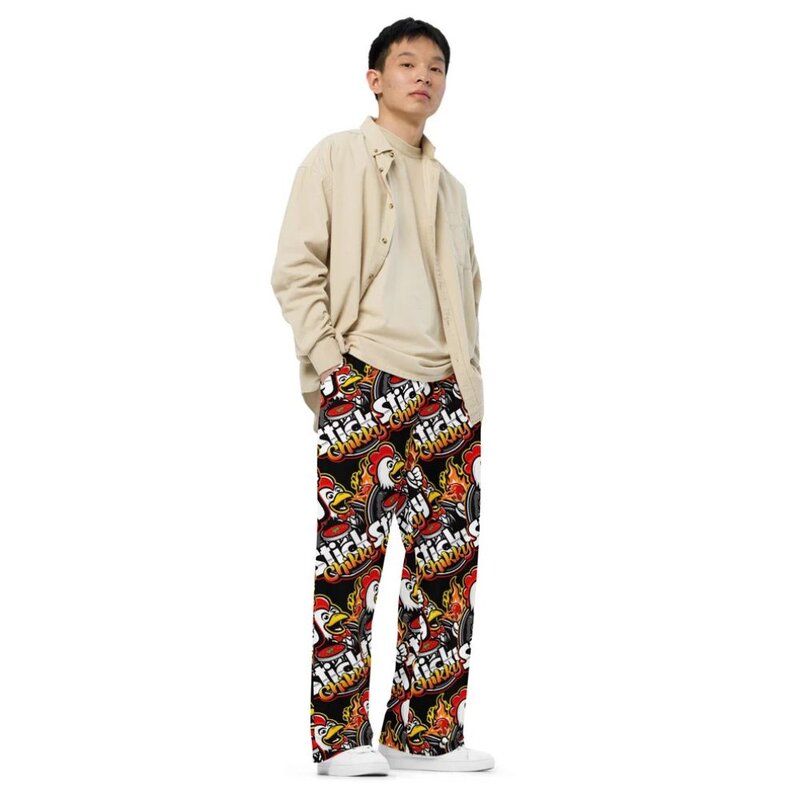 Man wearing wide-leg pants with an all-over print featuring repeated Sticky Chikky mascot logos and flame graphics in red, yellow, and black, white background