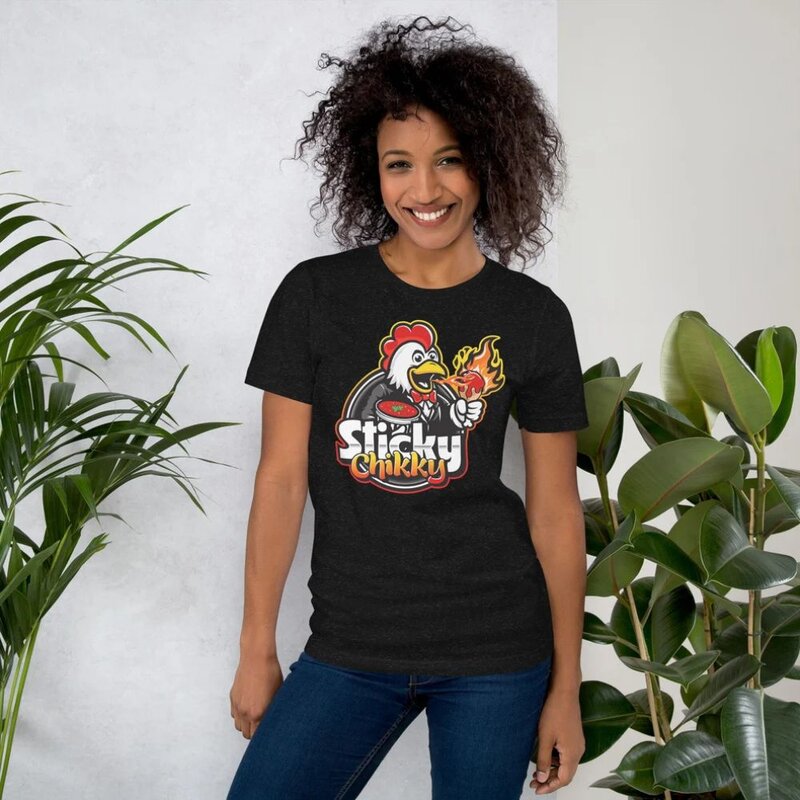 Woman smiling in a dark charcoal Sticky Chikky t-shirt with the mascot logo printed on the front, standing near houseplants
